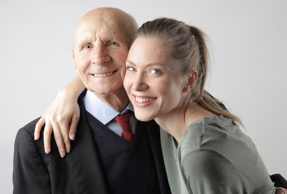 An adult daughter embracing her senior father, both smiling
